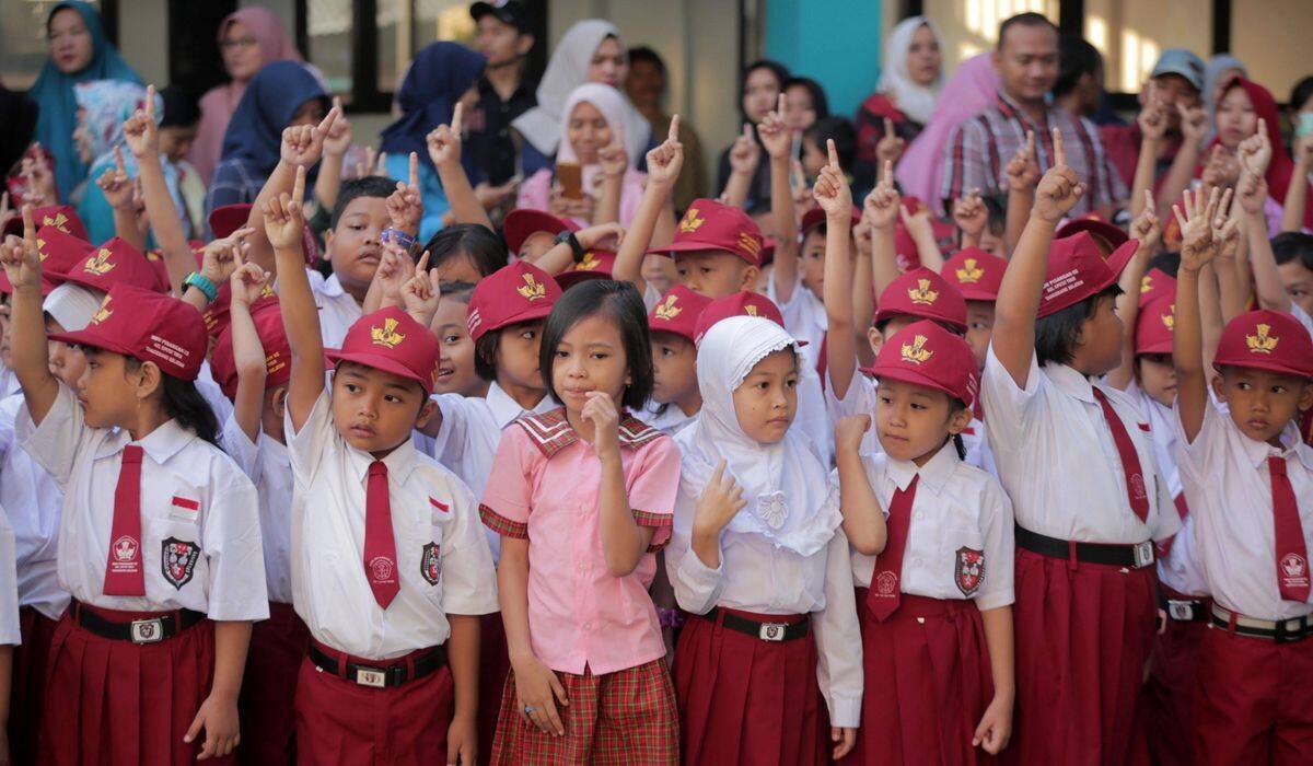Siswa SD berseragam merah putih dan bertopi mengangkat tangan dengan antusias