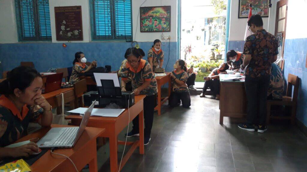 Guru di meja pendaftaran membantu orang tua mengisi formulir PPDB dengan laptop